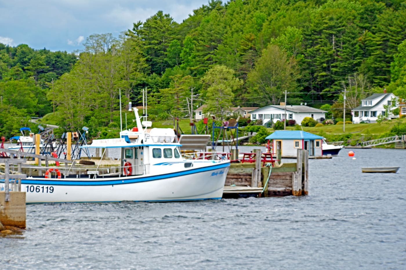 A fishing boat at a wharf in Mahone Bay, houses on the wooded shore behind